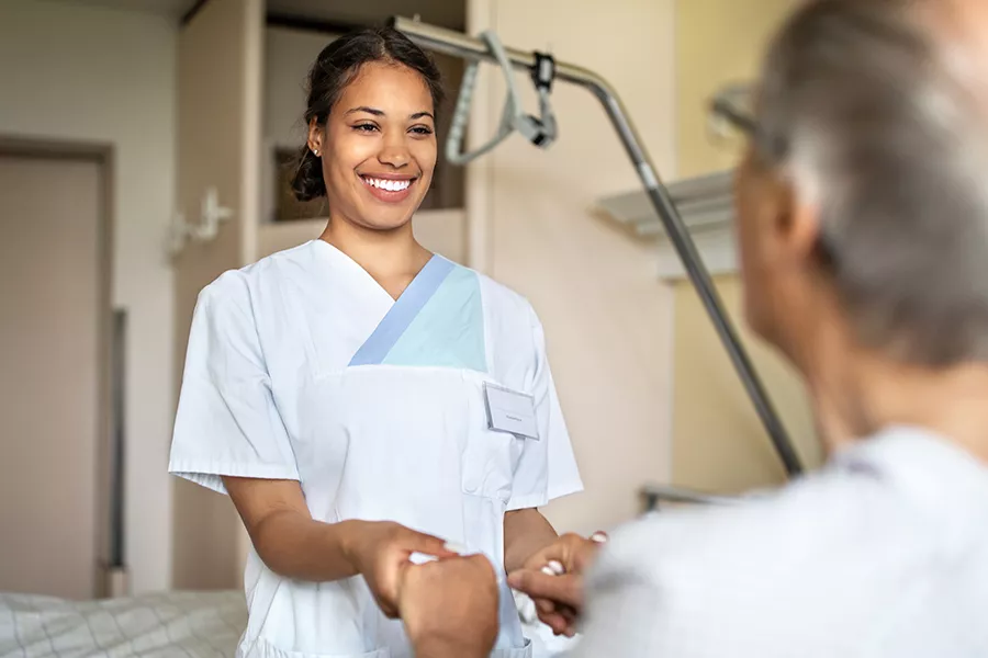 Verpleegkundige met client aan bed houden handen vast