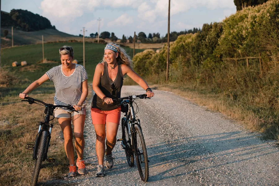 Twee vrouwen lopen met fiets in de hand lachent